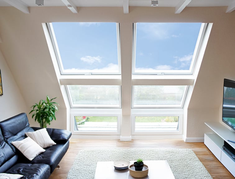 Wohnzimmer mit Sofa links und Fernseher rechts, mittig zwei Roto Dachfenster und davor ein Couchtisch auf einem Teppich.