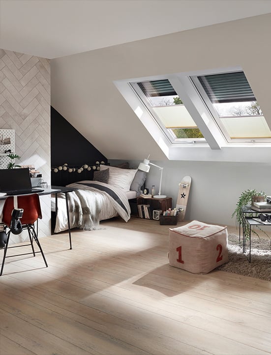 Jugendzimmer mit 2 Roto Dachfenstern und Ausstattung beinhaltet ein Bett unter der Dachschräge, einem Schreibtisch, einem Couchtisch und einem Sitzwürfel.