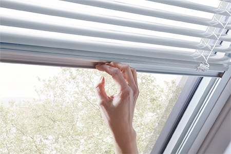 Hand schließt Jalousette, welche innen am Roto Dachfenster angebracht ist