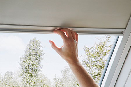 Hand schließt ein Verdunklungsrollo, welches innen an einem Roto Dachfenster angebracht ist