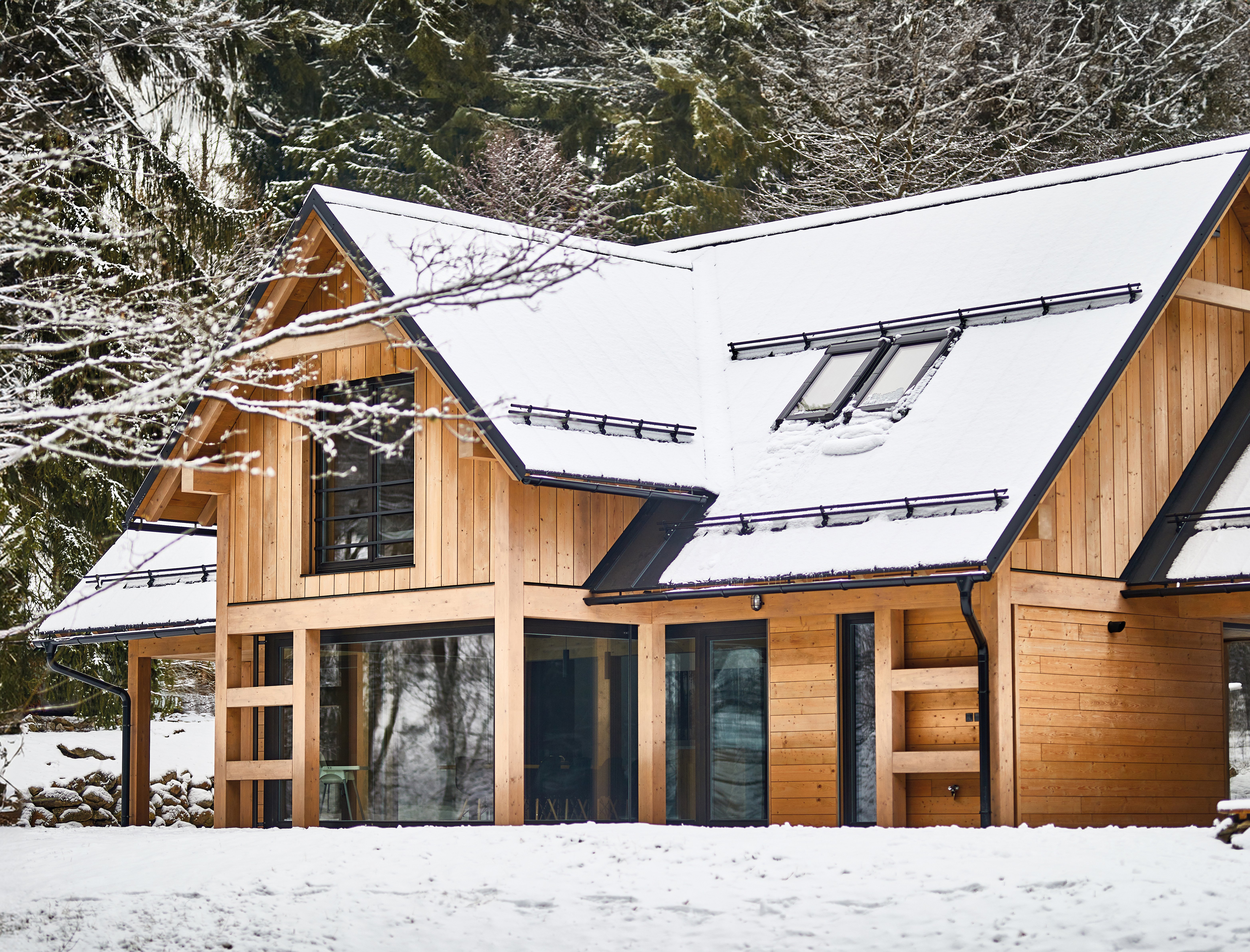 Holzhaus am Waldrand im Winter mit schneebedecktem Dach